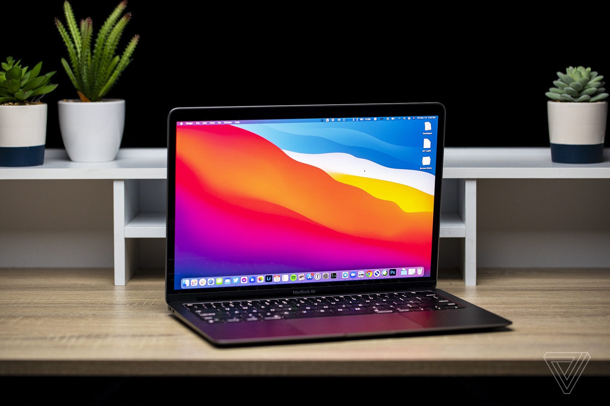 The M1 MacBook Air sitting on a desk with a shelf and three plants behind it.